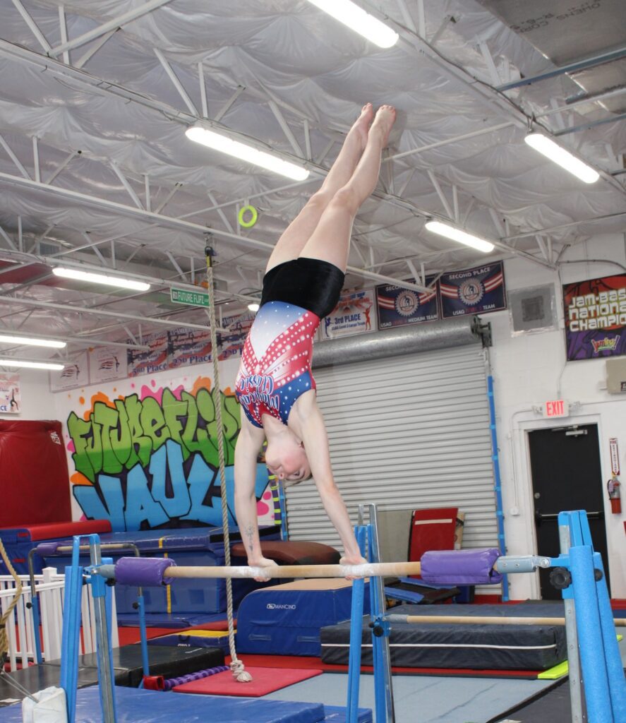 Gymnast performing a handstand on parallel bars indoors.